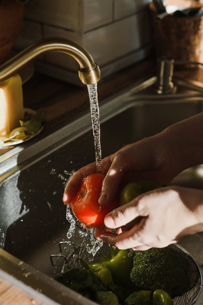 Close-up of hands washing a ripe tomato under a kitchen faucet. Perfect for themes of cleanliness and healthy living.